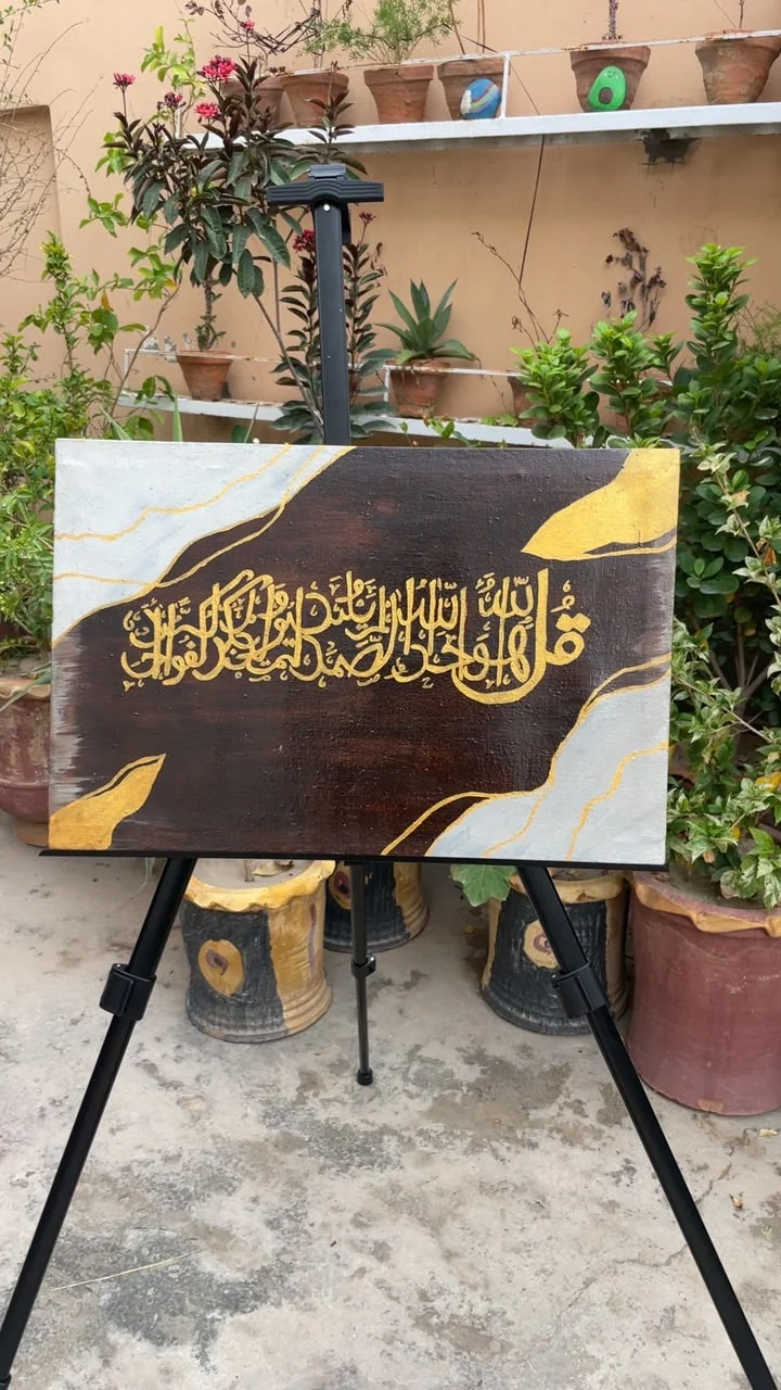 Gold Arabic calligraphy painted on a dark canvas with white and gold corner details