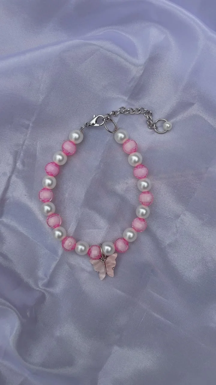 Pink and white beaded bracelet with a butterfly charm on soft lavender fabric