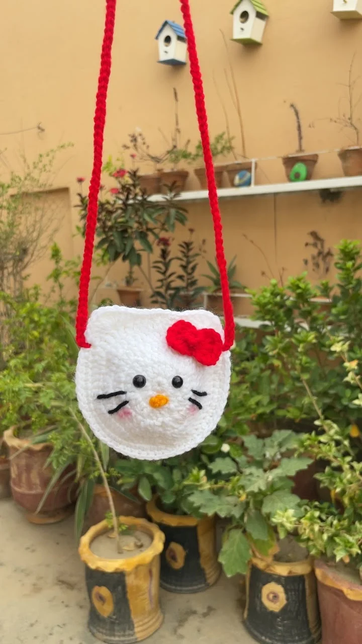 Small white crochet cat-face bag with a red bow and red shoulder strap